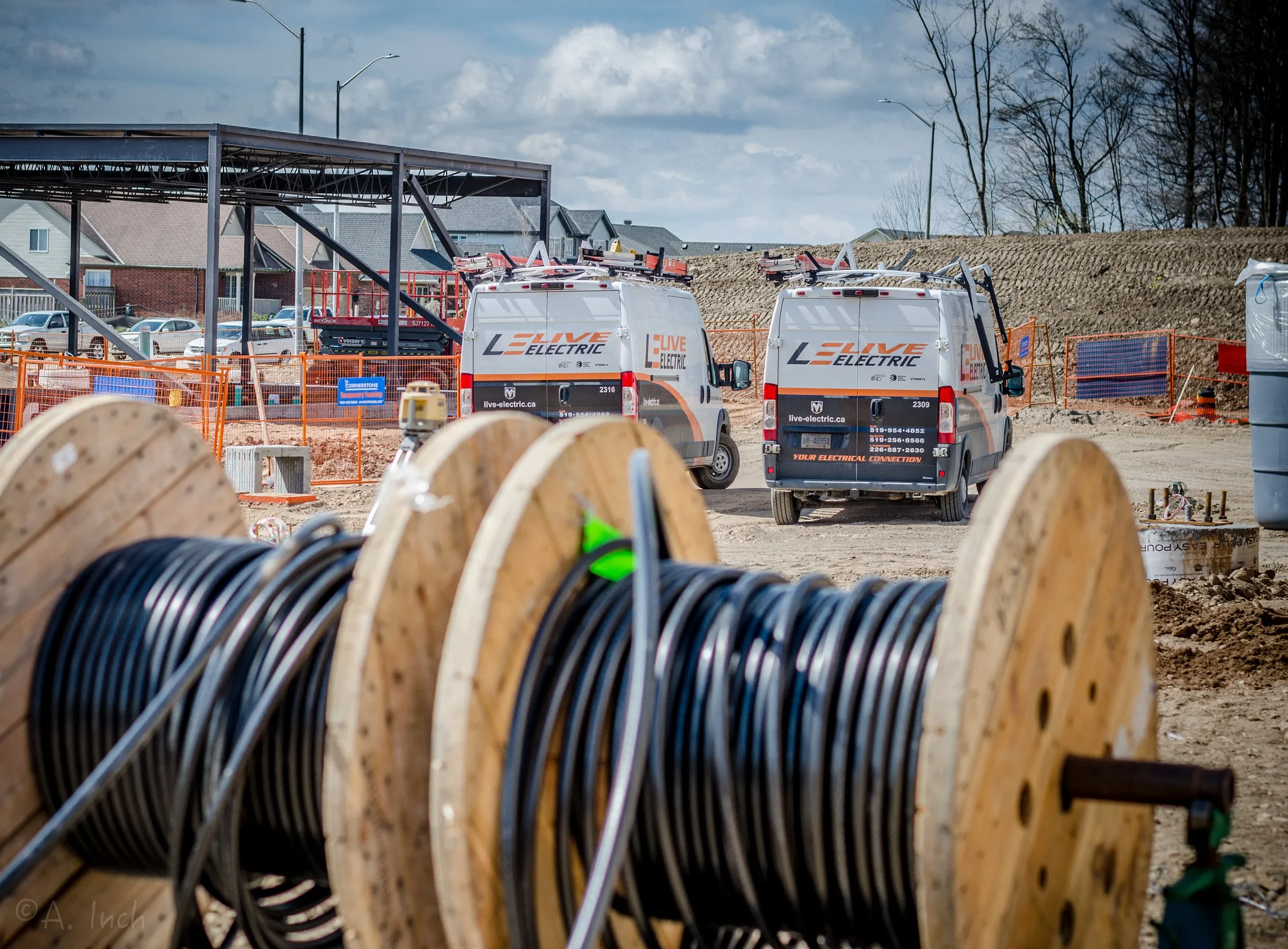 Reels of electrical cable in the foreground with two Live Electric vans on a construction site behind