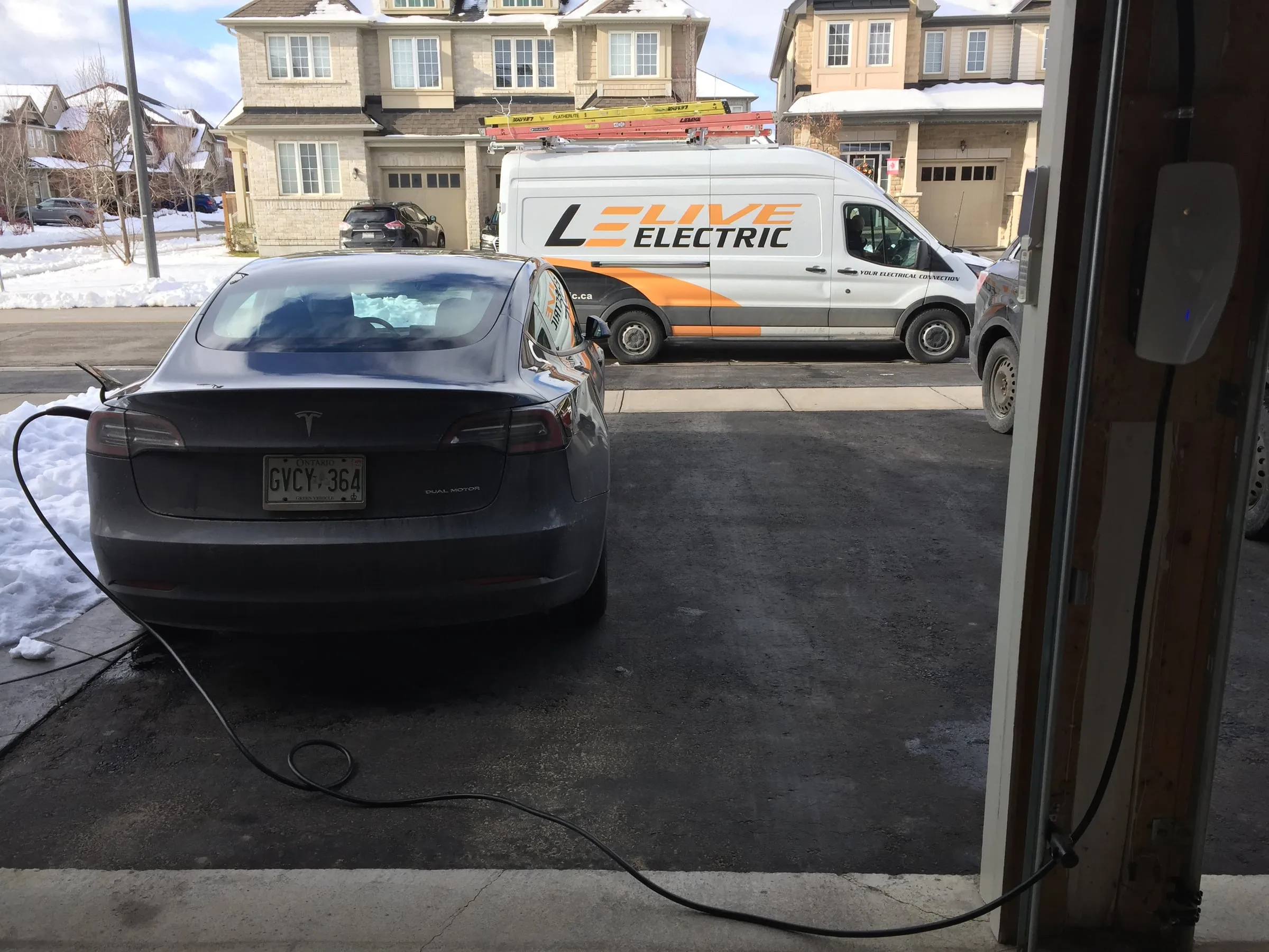 Tesla plugged into a newly installed home charger in a driveway with a Live Electric van behind