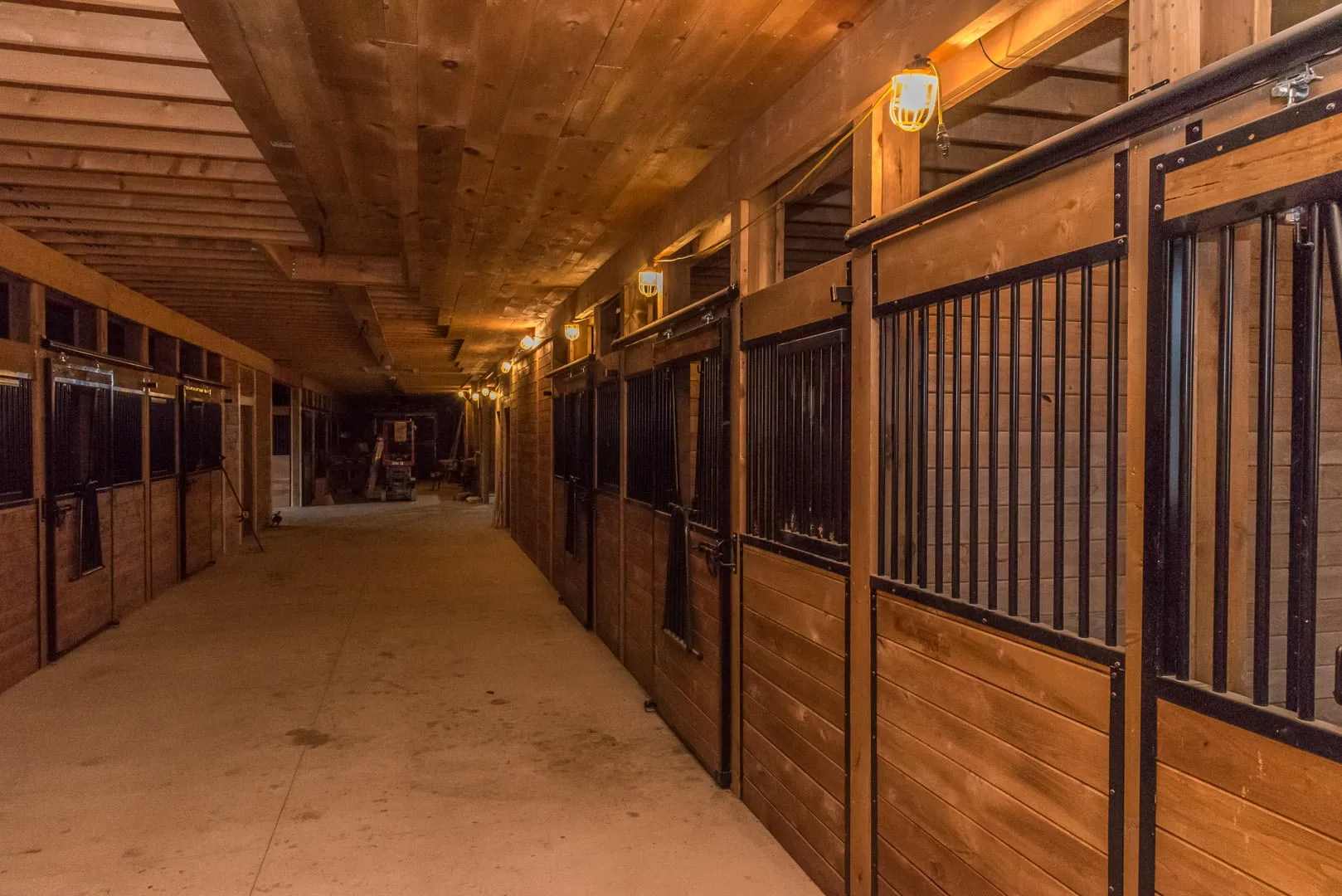 Long stall aisle inside a horse barn lit by ceiling fixtures