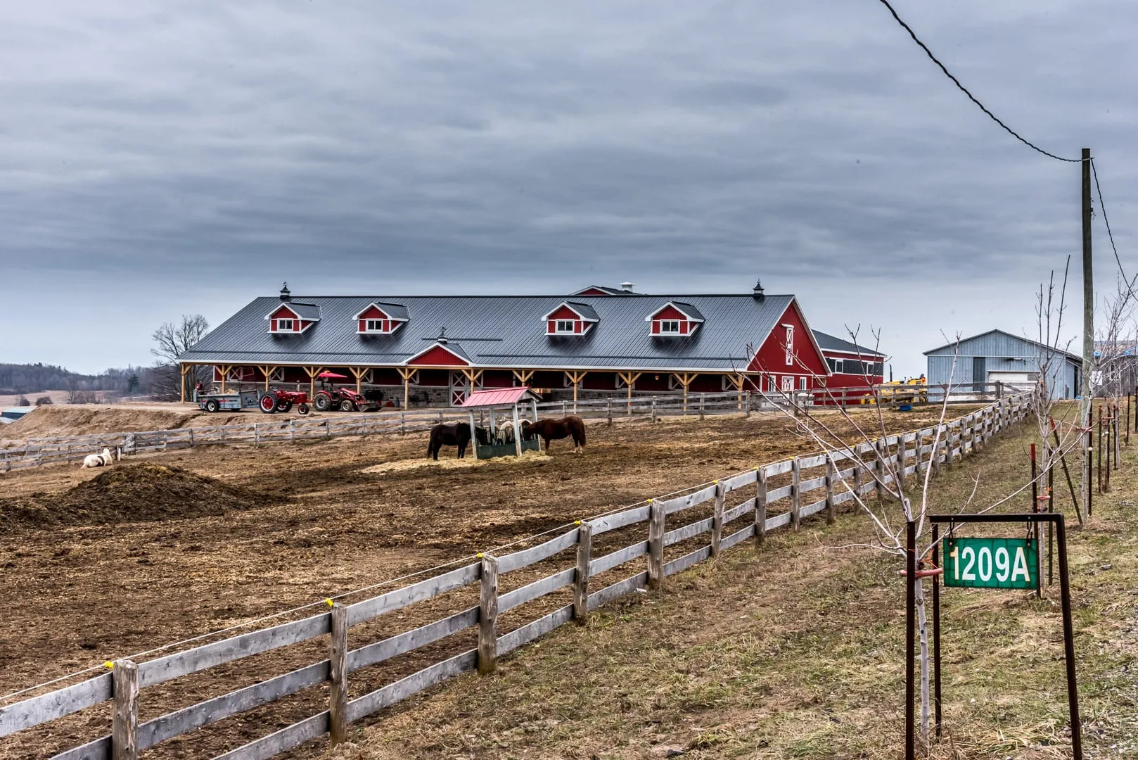 Red-and-stone horse barn exterior with paddock fencing and horses