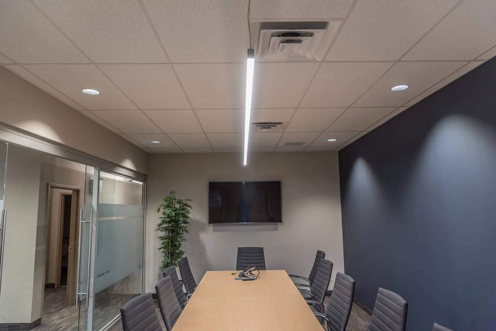 Renovated boardroom with a long table, linear pendant light and wall-mounted display